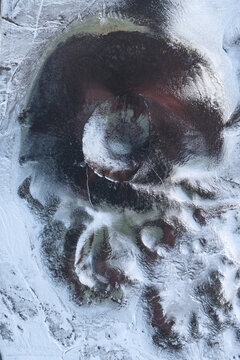 Aerial view of a snow-covered volcanic crater with dark rock formations and rugged terrain in Iceland.