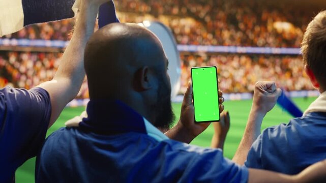 Close up of mockup smartphone used by man in soccer stadium stands to compare match odds, showing football supporter checking live score application predictions on chroma key phone.