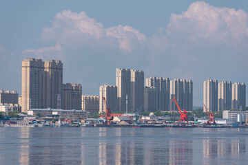 Modern Heihe waterfront with tall residential towers, port cranes, and reflective river foreground © Mikhail Mishchenko
