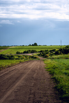 Dirt road winding through lush green fields under a partly cloudy rural sky
