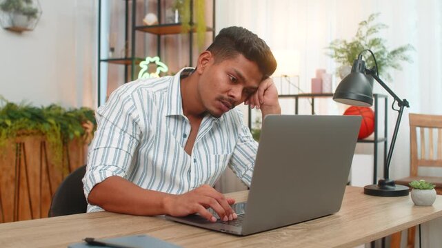 Indian man at home shuts laptop with fast hand says enough and breathes out and wants time without tech. Arabian guy at desk looks aside rubs neck and plans short pause for focus recovery and mind zen