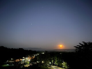 Obraz premium Moonrise over a quiet rural landscape with distant hills, village lights, and a starry evening sky viewed from an elevated viewpoint in a peaceful, inspiring atmosphere.