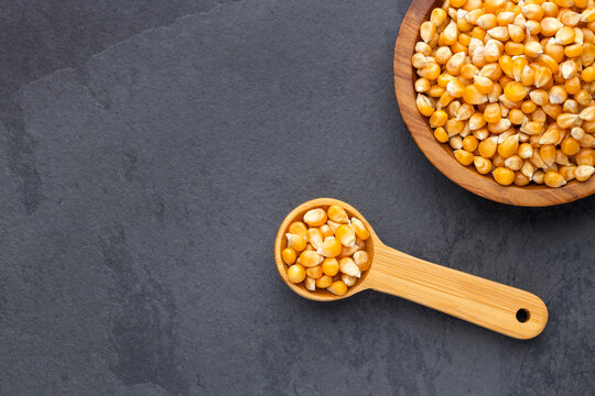 Popcorn kernels presented in wooden utensils on a dark surface, ideal for food and cooking concepts