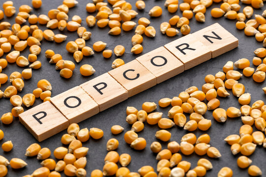 Popcorn represented with corn kernels and wooden letters on a dark background, snack, film, and food concept