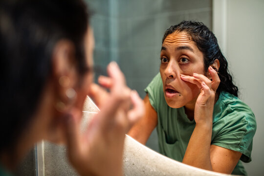 Woman examining dark circles in bathroom mirror at home