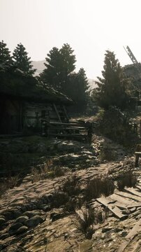 A path winds through a rural area filled with old buildings and trees. The sun rises, casting light on the stones and plants along the way.