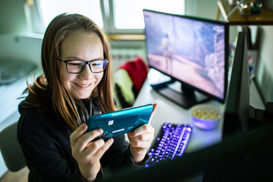 Smiling teen gamer playing smartphone at home desk