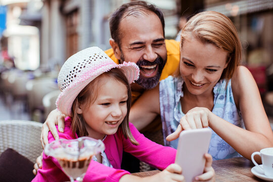 Happy family looking at smartphone at outdoor cafe