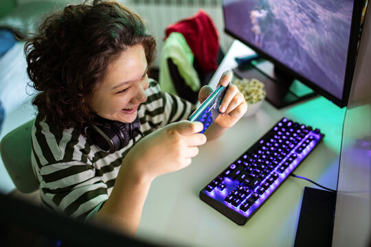 Smiling teen playing smartphone game at home gaming setup