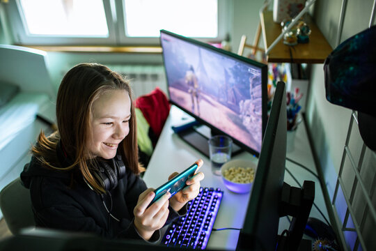 Teen girl gaming on smartphone at home desk