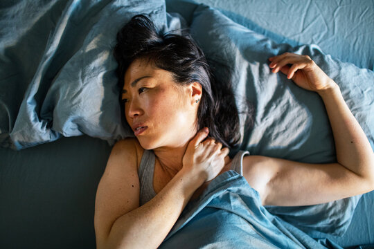 Woman with neck pain awake in bed at home