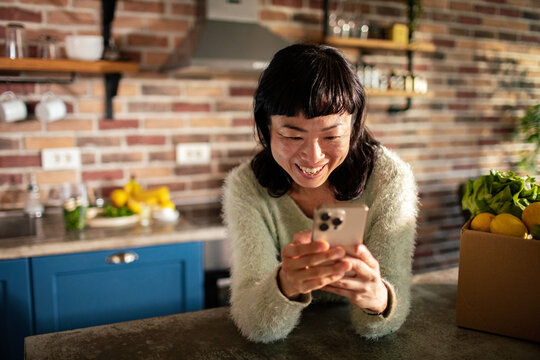 Smiling woman using smartphone in cozy home kitchen