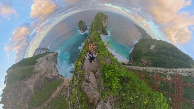 Spherical Panorama of Two Tourists Walking Down Narrow Cliff Ridge Toward Kelingking Beach on Nusa Penida, Coastal Adventure Travel
