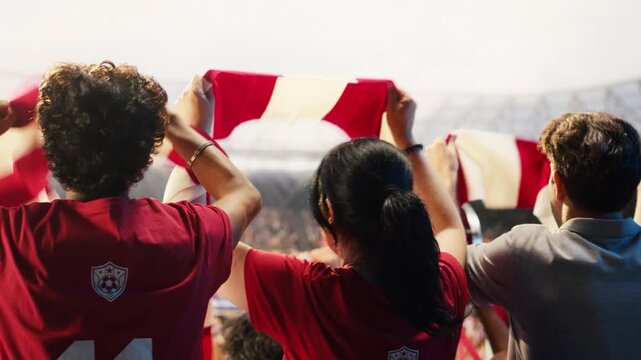 Rear view of happy supporters cheering under falling confetti after football goal, showing back view of cheerful soccer fans celebrating tournament match final win in stadium for fan culture content.