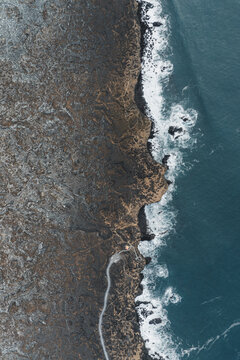 Aerial view of rugged volcanic lava fields meeting the dark Atlantic Ocean waves along the dramatic coastline of Iceland.
