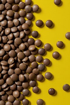 Brown lentil seeds scattered across a bright yellow background. These tiny legumes offer plant based protein essential for healthy diets. Perfect for food blogs and recipes.