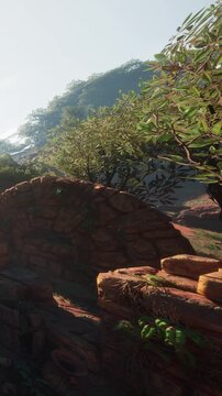 The scene shows a set of old stone ruins surrounded by trees and greenery. The sun shines on the landscape, highlighting the natural features and structures.