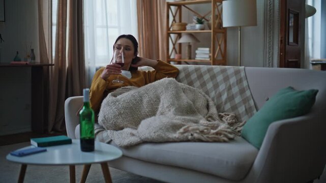 Depressed lady drinking wine sitting living room couch. Unhappy brunette sipping