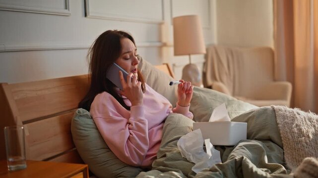Unwell lady speaking cellphone resting bed checking thermometer suffering fever.