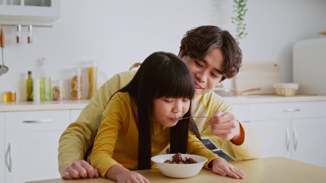 Joyful Smiling Asian Girl Enjoying Breakfast With Her Father, Sitting Together At Kitchen Table In Bright Modern Kitchen. Positive Family Bonding Moment, Capturing Love And Togetherness.