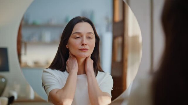 Brunette performing facial massage looking mirror at beauty ritual home closeup.