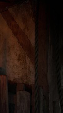 A wooden structure stands against a wall in a dimly lit area. Ropes hang from the structure, creating a strong visual presence. The atmosphere is simple and focused on the materials used.