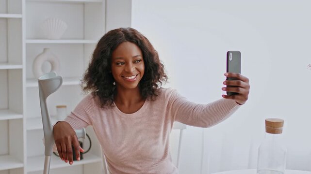 Smiling Black Woman Taking Selfie With Smartphone While Sitting At Home, Enjoying Moment In A Bright Living Room Setting, Feeling Cheerful And Engaging In Modern Lifestyle Concept.