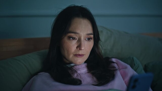 Unhappy lady lying bedroom holding smartphone feeling stressed nighttime closeup