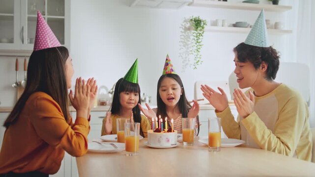 Joyful Children Smiling While Celebrating Birthday Together With Family At Kitchen Table, Clapping Hands Around Cake With Lit Candles. Fun Family Gathering In Cozy Home Setting.