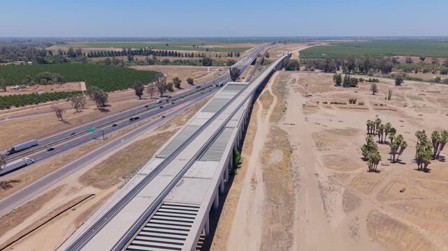Reversing and Panning Aerial Drone Shot Right to Left Over California High Speed Rail Construction With Overpass Freeway Traffic Palm Trees and Farmland