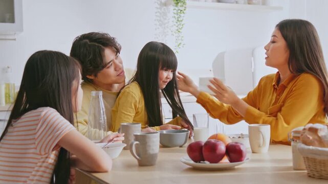 Joyful Multiracial Family Of Four, Including Two Women And Two Men, Sitting Together At Kitchen Table Eating Breakfast, Sharing Laughter And Happy Moments In A Cozy Home Setting. Family Concept.