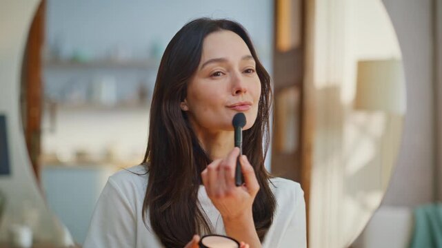 Girl using makeup brush applying powder looking home mirror closeup. Lady makeup