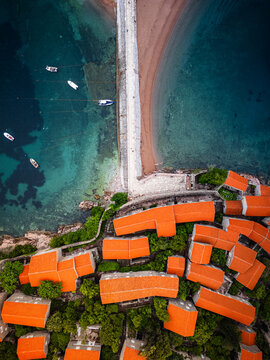 Aerial view of the historic Sveti Stefan resort featuring orange-tiled rooftops, stone causeway, and turquoise Adriatic Sea waters in Sveti Stefan, Budva Municipality, Montenegro.