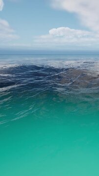 Waves gently roll in the ocean under a blue sky. The water shows different shades of blue and green. Clouds float above in the distance.