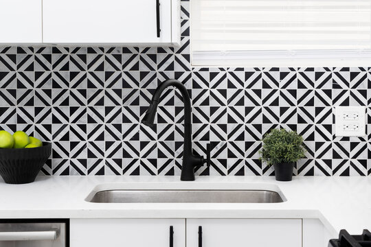 A black kitchen faucet detail with diamond black marquina and carrara white marble tile backsplash, white marble countertop, and white modern cabinets.