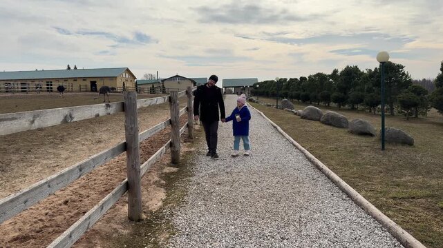 Little girl in a blue coat and her dad exploring a rural safari park on a bright spring day.