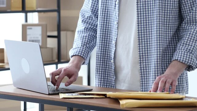 Man with postal envelopes working on laptop at table in office, closeup