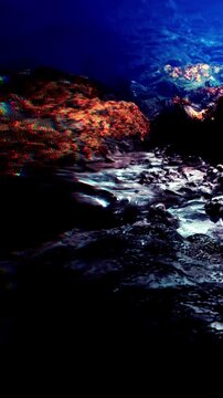 Water moves smoothly over rocky surfaces at night near the shore. The area shows shadows and reflections under the dark sky, creating a natural scene by the ocean.