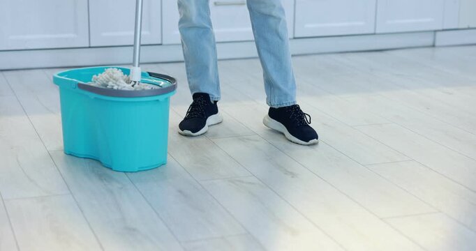 Housework. Teenage boy cleaning floor with mop in kitchen, closeup