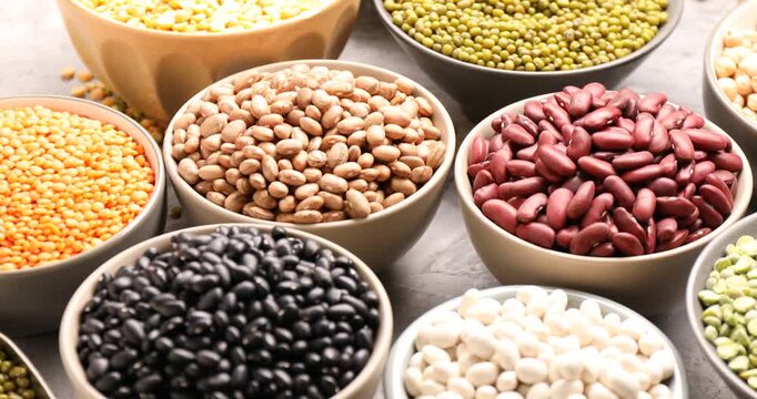 Different types of legumes in bowls on grey table, closeup. Camera moving