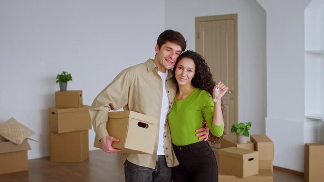 Happy Latin American Couple, Young Adults, Smiling While Holding Moving Box And House Keys In Their New Home. Excited Emotion In A Modern Setting, Celebrating New Beginnings, Moving Concept.