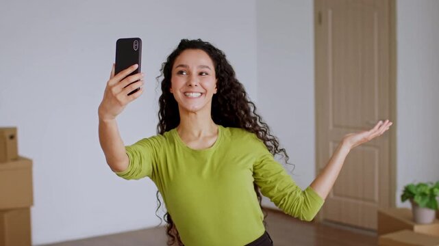 Smiling Young Middle Eastern Woman Taking Selfie While Standing In Living Room At Home, Showing Excitement And Joy For New Beginnings. Bright Indoor Setting. Lifestyle Concept.