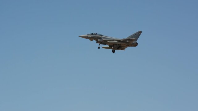 Fighter aircraft on approach with landing gear extended, external fuel tanks under the wings, single seat delta wing jet flying in clear blue sky, slow motion