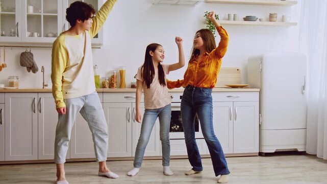 Cheerful Happy Family Of Three, Mother, Father, And Daughter, Dancing Joyfully Together In Modern Kitchen. Embracing Fun Moments With Laughter And Joy, Promoting Healthy Lifestyle And Exercise.