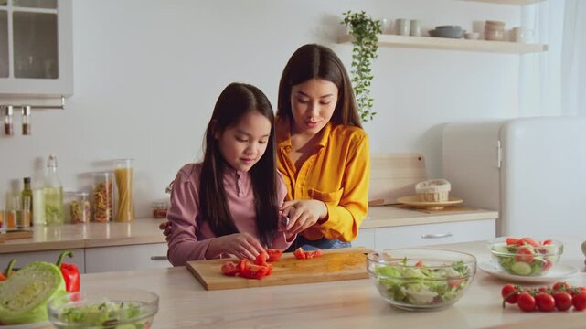 Smiling Asian Woman And Young Girl Engaged In Preparing Fresh Ingredients While Cooking Together In Bright, Modern Kitchen. Joyful Moment Of Bonding Over Healthy Meal Preparation.