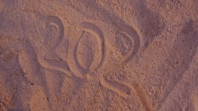 First Person View Finishing 2027 Written in Beach Sand With a Wooden Stick During Sunset, New Year Celebration, Future Plans, Fresh Start