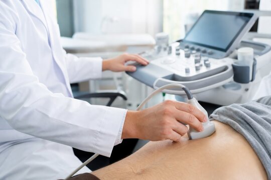 Sonographer performing abdominal ultrasound scan on male patient using modern diagnostic equipment in bright clinical hospital room, healthcare concept