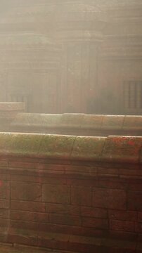 Visitors walk among stone structures shrouded in mist at a historical site in the early morning. The atmosphere is quiet as sunlight filters through the haze.