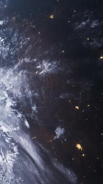 Earth from space during nighttime. City lights are visible as bright spots against the dark surface. Clouds and patterns of weather can be seen in the atmosphere.