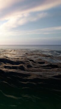 Water moves in gentle waves as the sun sets on the horizon. The sky shows colors of dusk, and the ocean reflects the light, creating a peaceful scene by the shore.